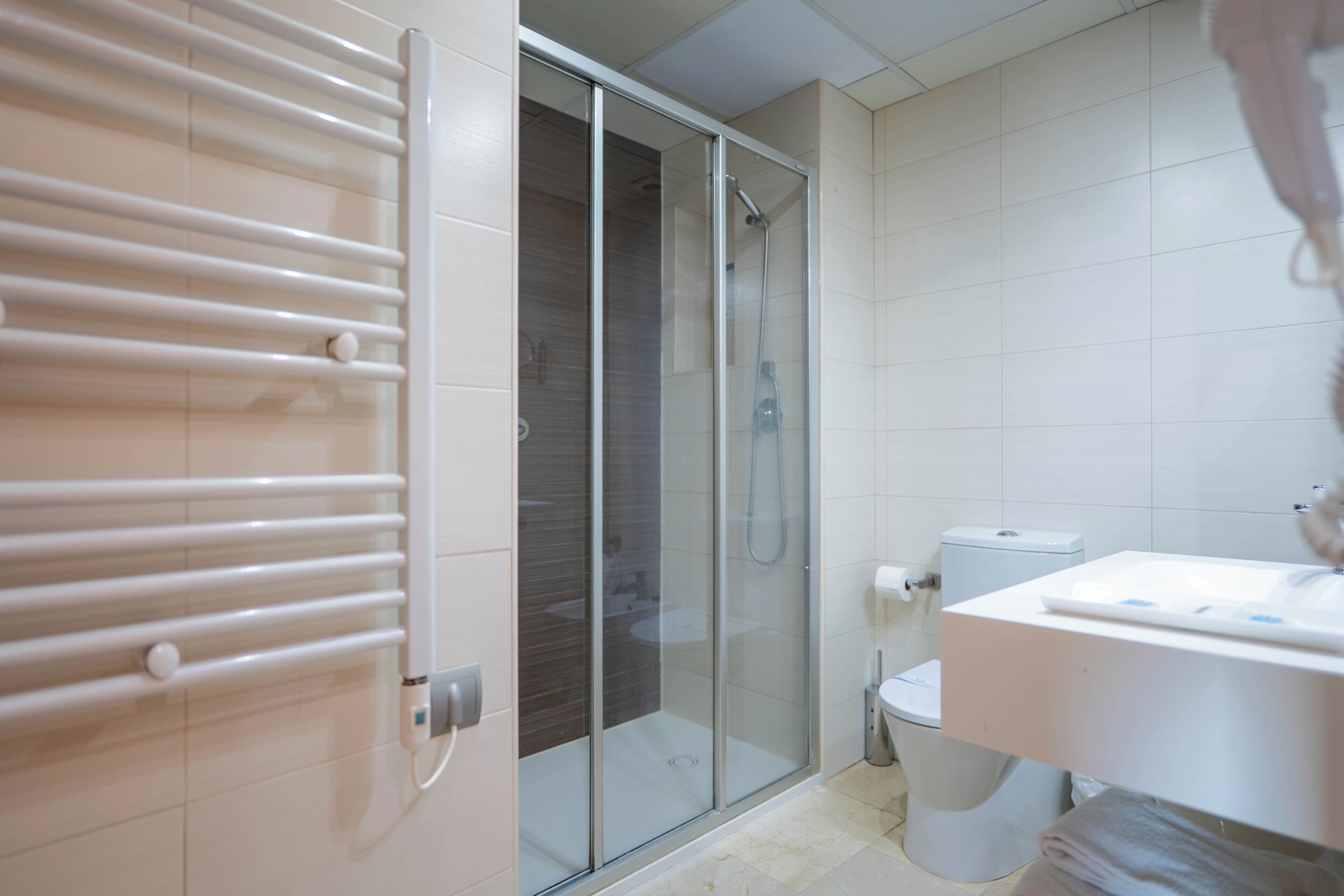 Un baño con cabina de ducha de vidrio, inodoro y lavabo con toalla.