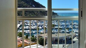 Vista a través de una ventana de un puerto deportivo con barcos, una montaña y cielo despejado.