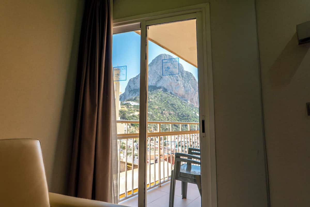 A hotel room with a balcony, a view of a mountain, and a chair outside.