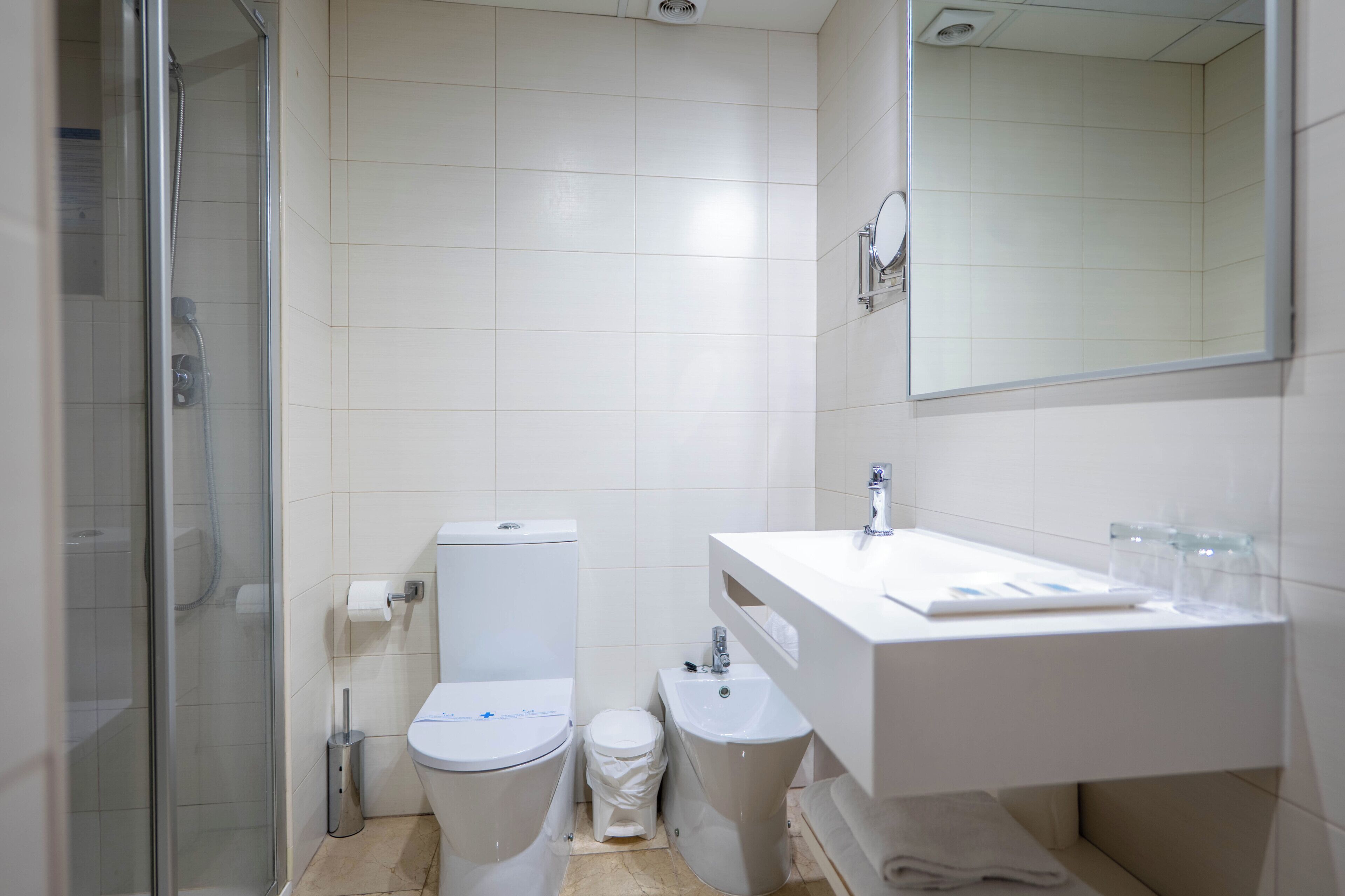 Un baño moderno con cabina de ducha de vidrio, inodoro blanco, bidé y tocador con espejo.
