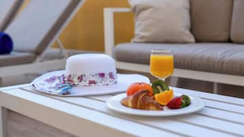 A breakfast setup with a croissant, orange, and strawberries on a plate, a glass of orange juice, and a patterned hat on a white table.