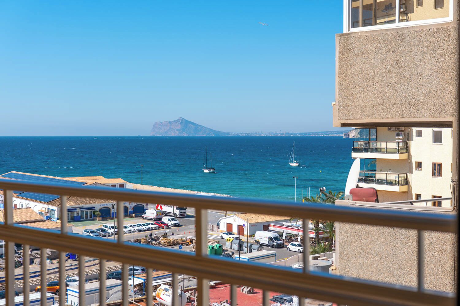 A coastal view with a mountain, boats, and a building with balconies.