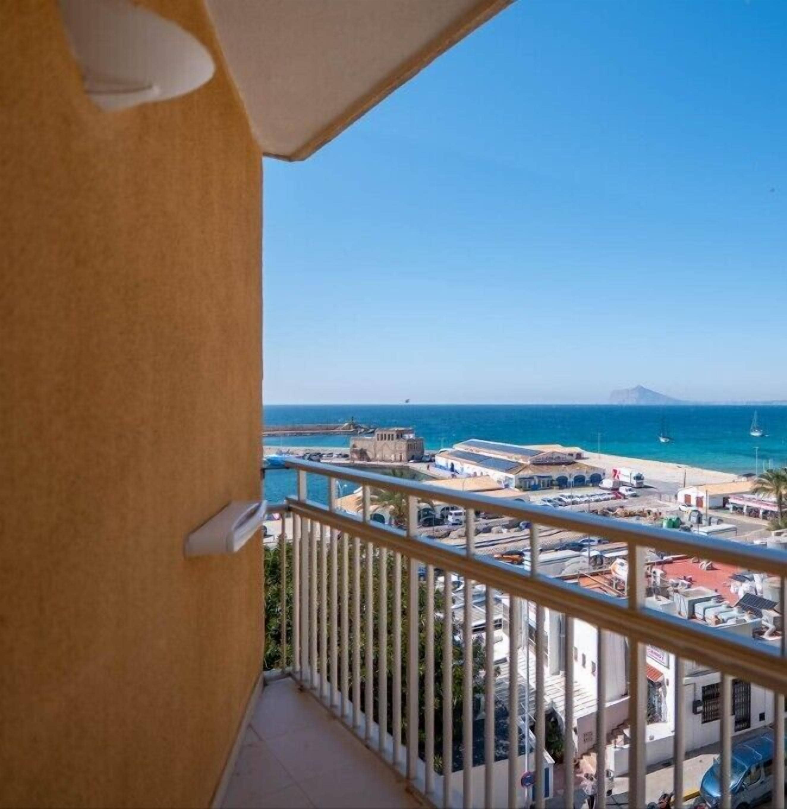 A balcony with a view of a coastal town, including a beach, boats, and a mountain in the distance.