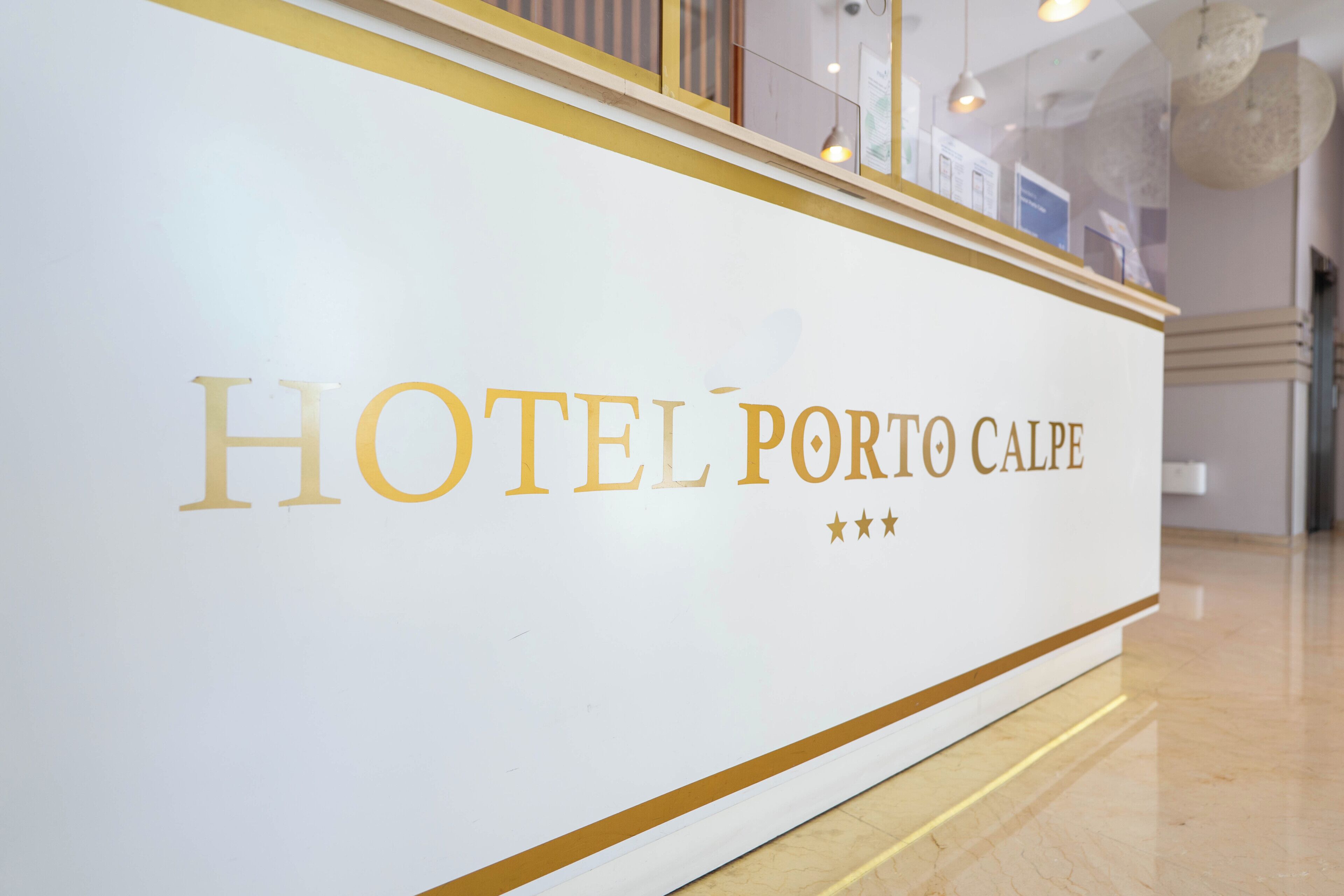 Un comptoir d’accueil blanc avec l’inscription « HÔTEL PORTO CALPE » et trois étoiles.