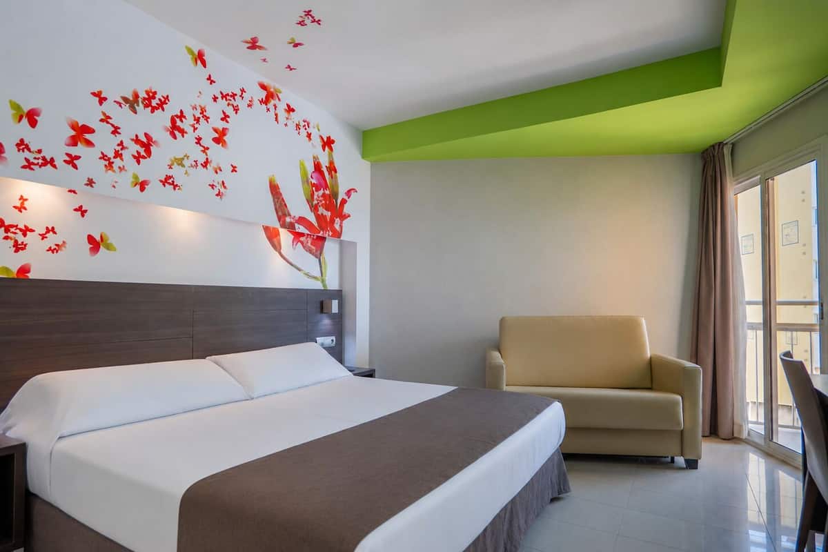 A hotel room with a bed, a chair, a nightstand, and a wall with butterfly decals.