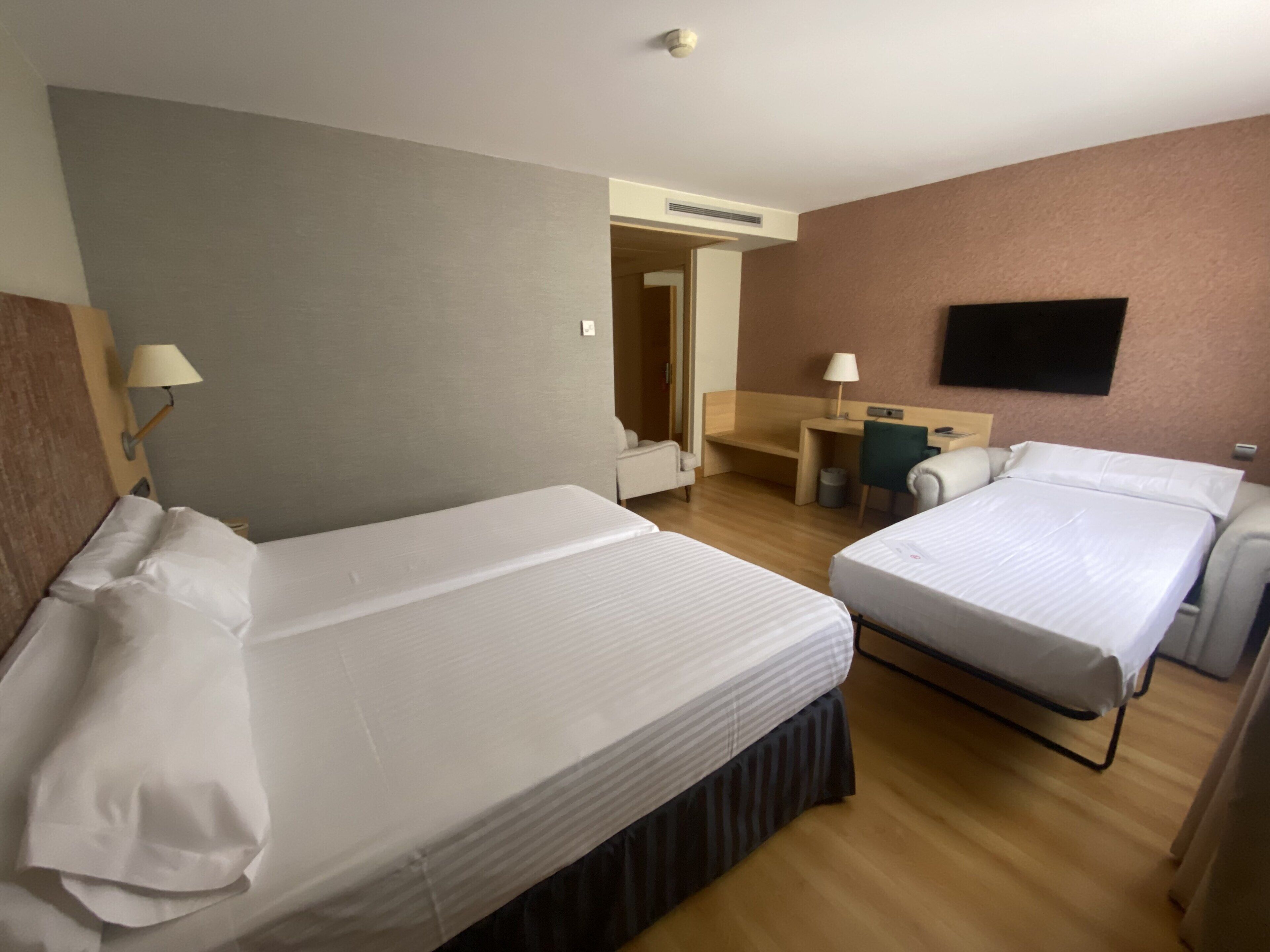 Une chambre d’hôtel avec deux lits, un bureau, une chaise et un téléviseur fixé au mur.