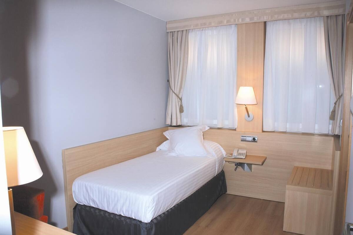 Una cama individual con cabecera de madera, una mesita de noche con lámpara y un teléfono.