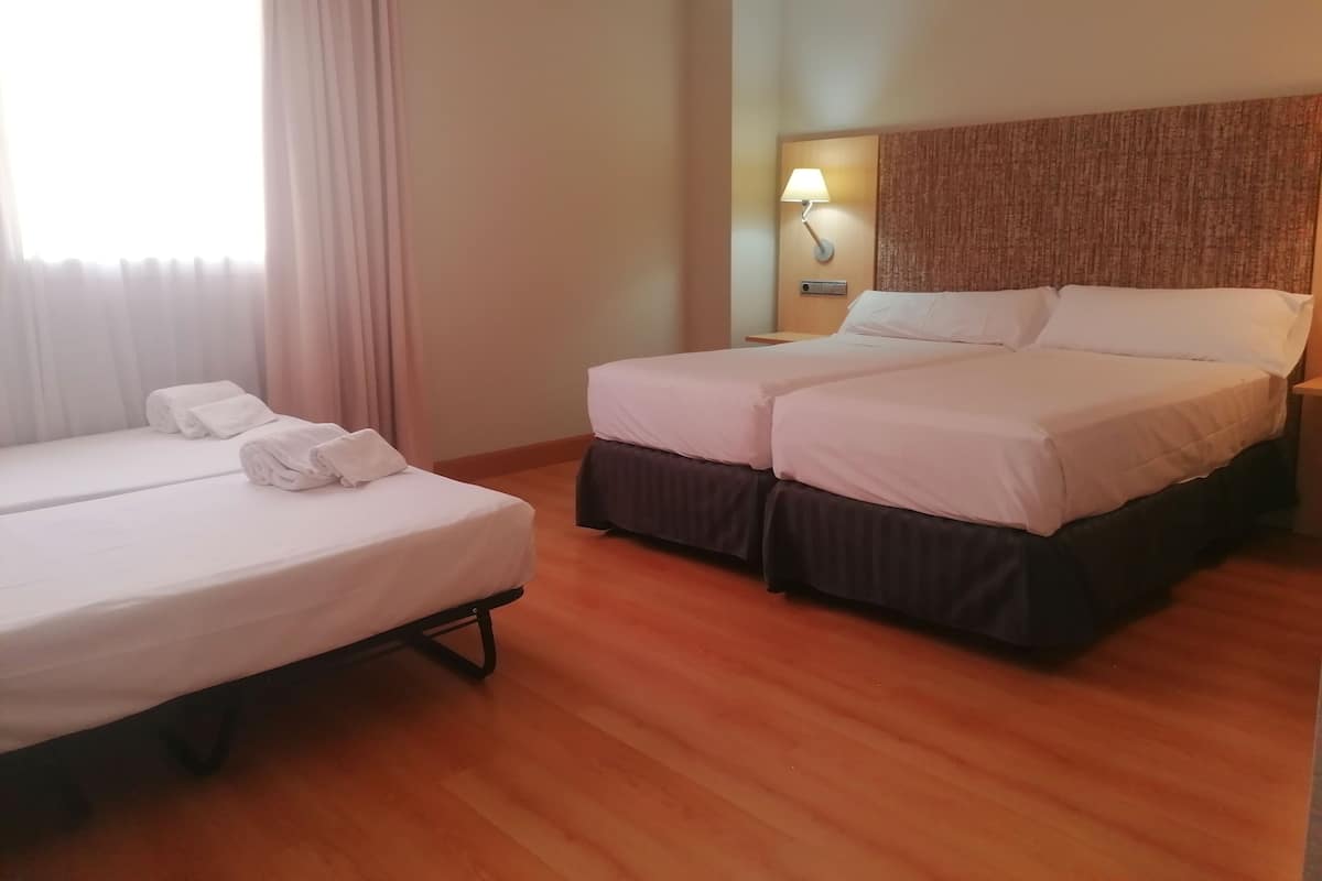 Una habitación de hotel con dos camas, una mesita de noche con lámpara y un ventanal con cortinas.
