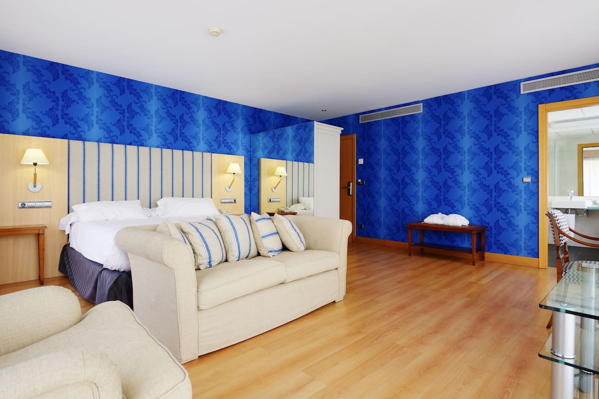 Una habitación de hotel con cama, sofá, mesa de vidrio y banco.