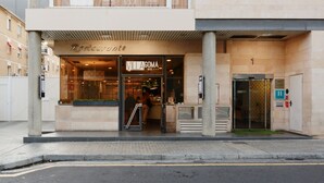 Entrada de hotel con fachada de vidrio, una recepción visible y una escalera que conduce al acceso.