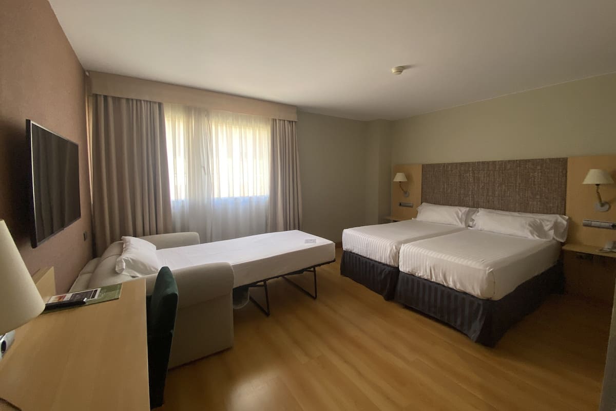 Habitación de hotel con dos camas, un escritorio, una silla, un televisor y una ventana con cortinas.