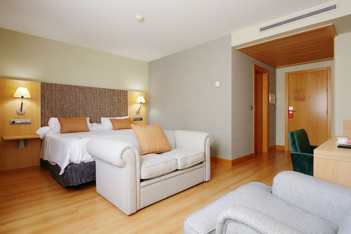 Una habitación de hotel con una cama, dos mesitas de noche con lámparas, un sofá, un escritorio y una silla.