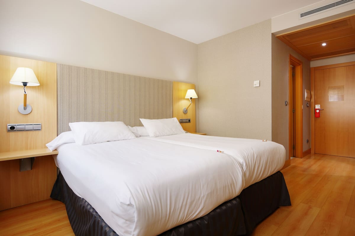 Una habitación de hotel con una cama grande, dos mesitas de noche, una lámpara de pared y una puerta de madera.
