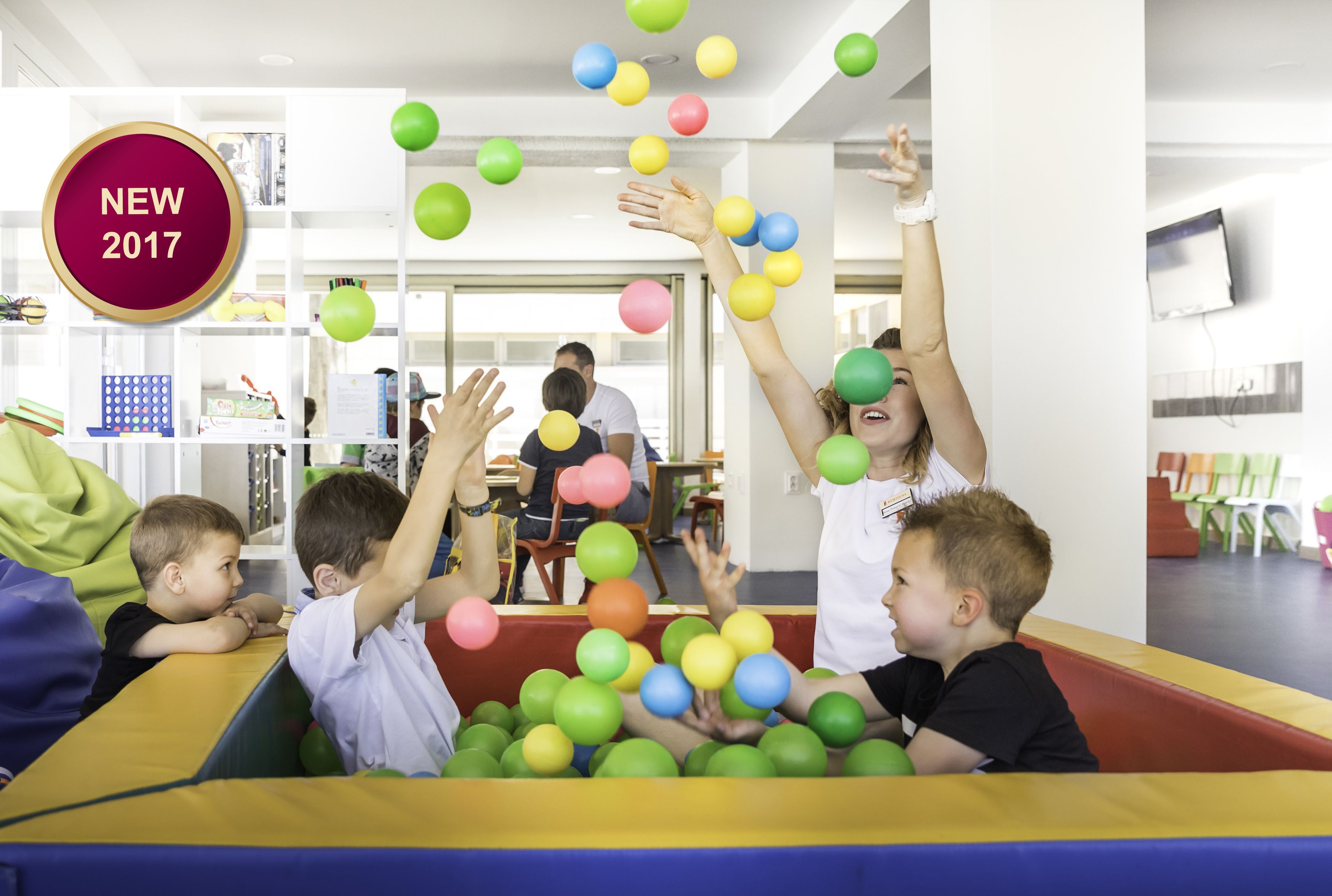 Children playing with colorful balls in a room with white walls and a television mounted on the wall.