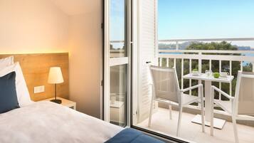 Ein Hotelzimmer mit Bett, Nachttisch mit Lampe und Balkon mit Tisch und Stühlen.