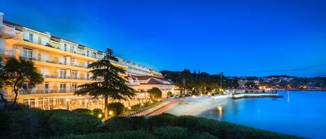A waterfront hotel with multiple balconies, a beach area, and a calm sea.