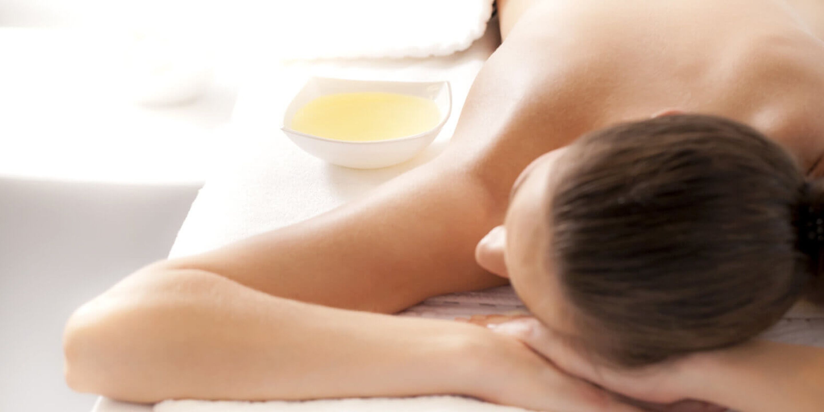 Eine Person bekommt eine Massage, auf dem Tisch steht eine Schüssel mit Öl.