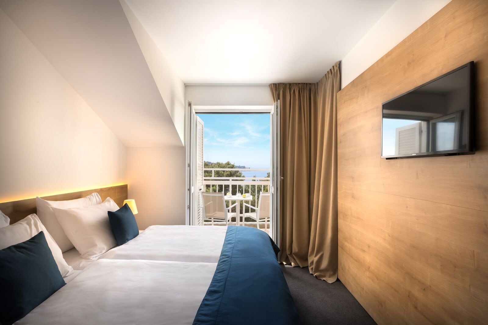 Una habitación de hotel con una cama, un televisor montado en la pared y un balcón con vistas.
