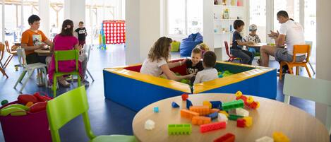 A brightly lit indoor play area with colorful play structures, seating, and a variety of toys.