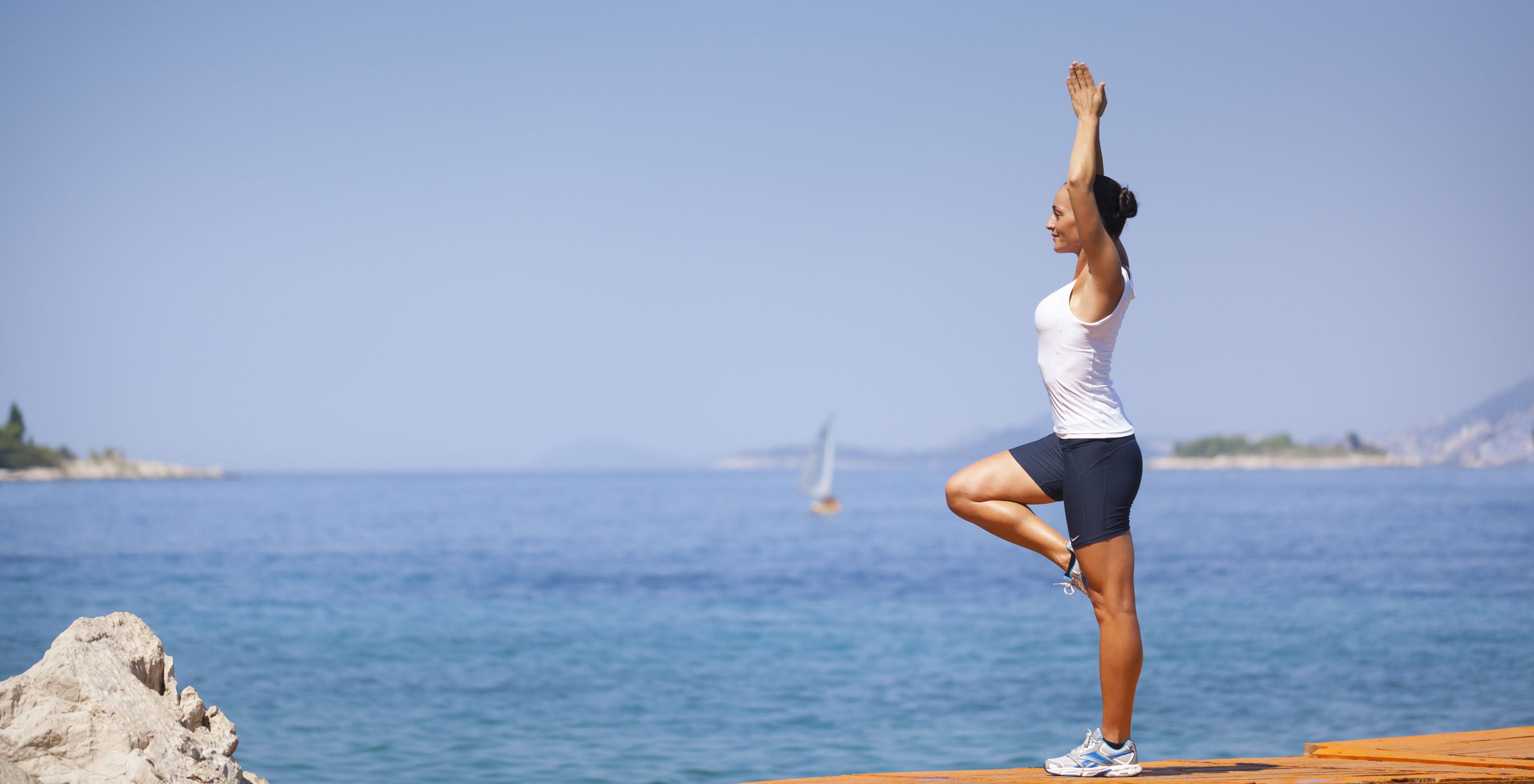Una persona esegue una posa yoga su un molo di legno vicino al mare.