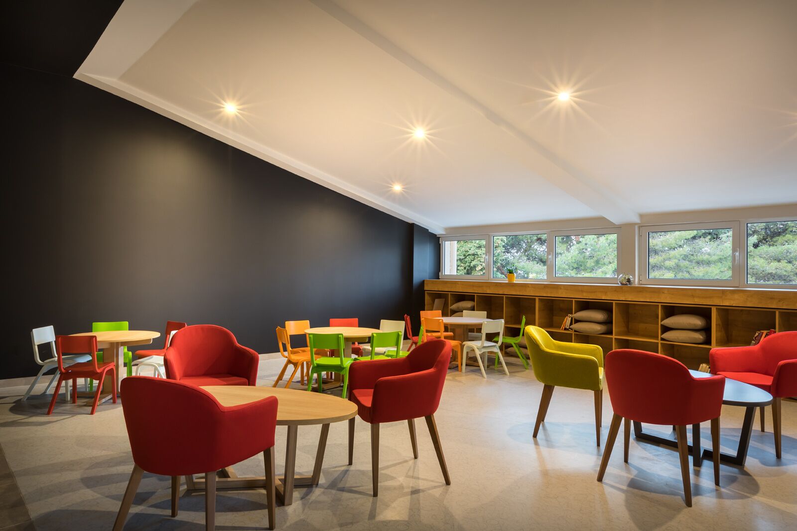 Een modern interieur met kleurrijke stoelen en tafels, een donkere accentmuur en uitzicht door grote ramen.