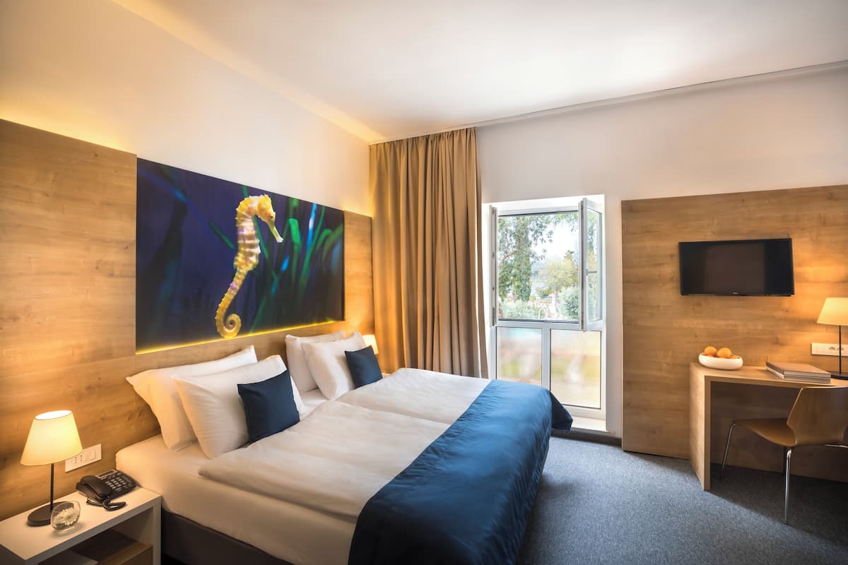 A hotel room with a large bed, a desk with a chair, a television, and a window with curtains.