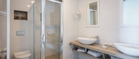A modern bathroom with a glass shower enclosure, a white toilet, and a vanity with a large sink and mirror.