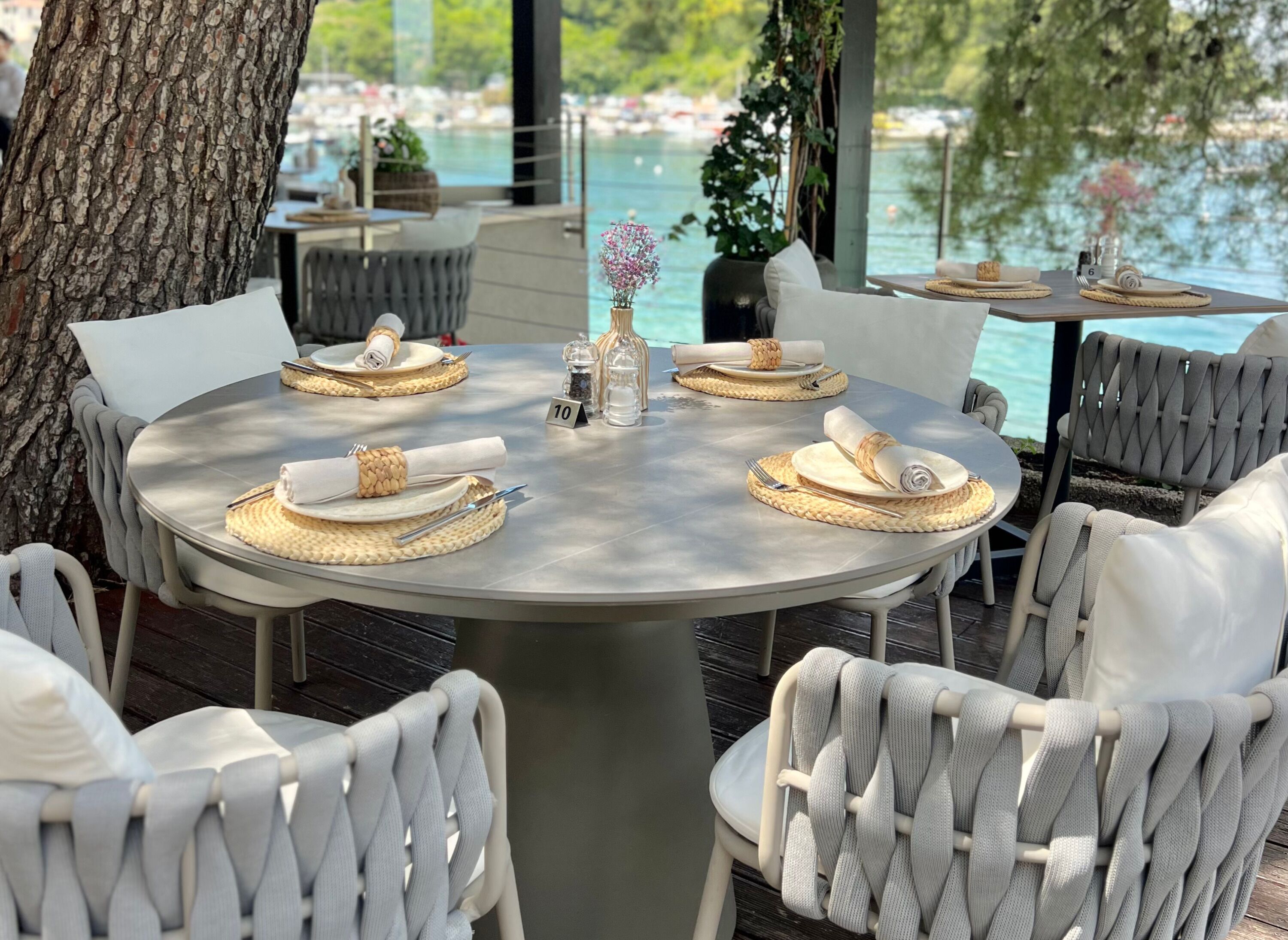 Une table de salle à manger ronde, entourée de chaises blanches, mise avec des assiettes, des couverts et des sets de table en fibres tressées.
