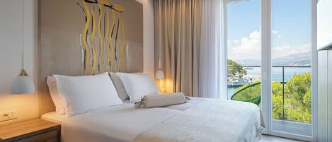 A hotel room with a bed, nightstand, lamp, and a view of a body of water through large windows.