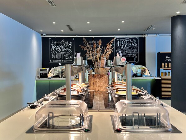 A buffet setup with clear signage for orange juice and hot cocoa, a central decorative vase, and a counter with various food items.