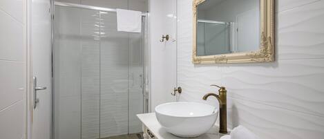 Un baño moderno con cabina de ducha de vidrio, un lavabo blanco con grifo dorado y un espejo grande con marco ornamentado.