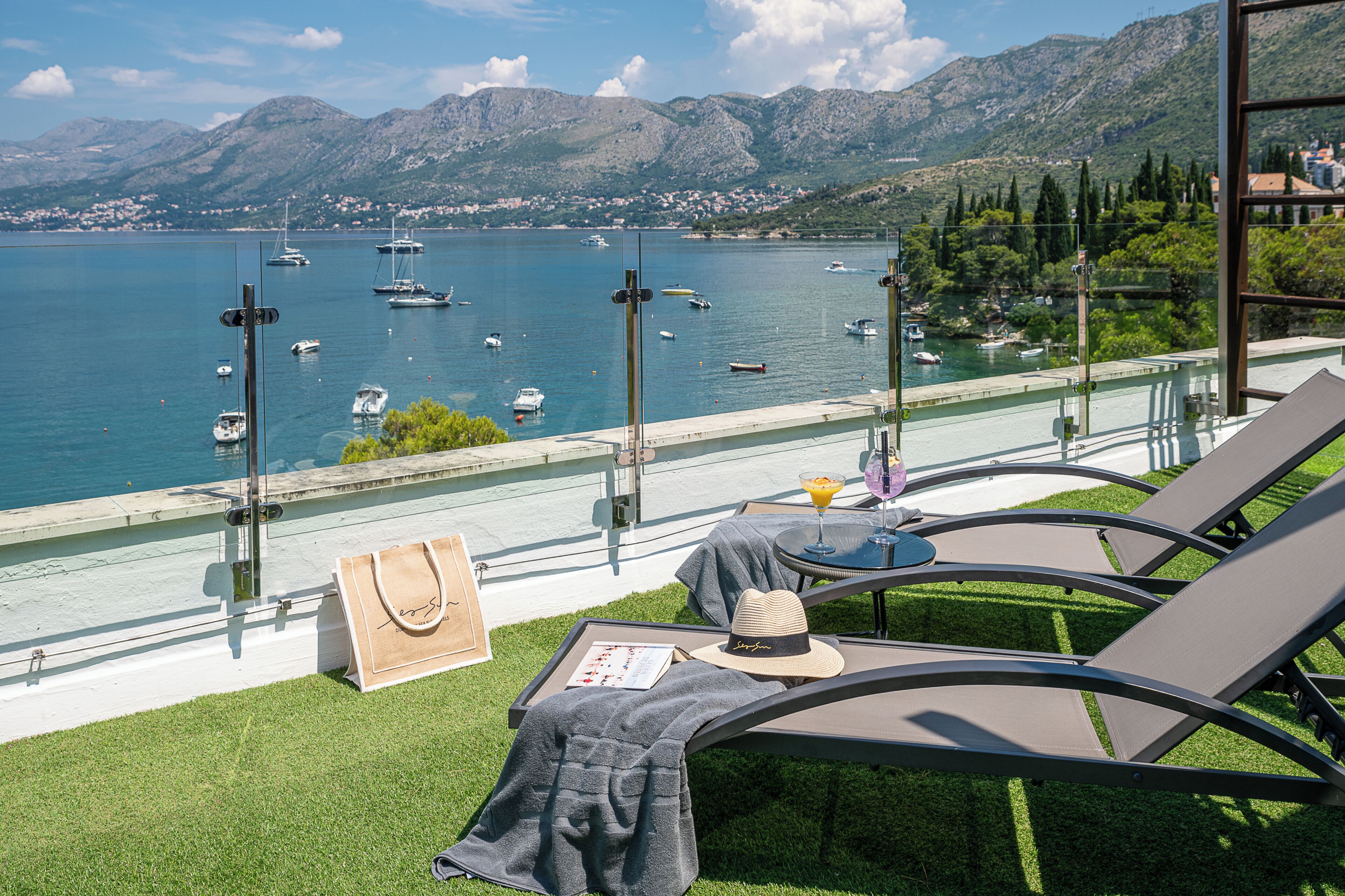 Una terraza con vistas a un lago, sillas de descanso, una mesa con una bebida y un bolso.