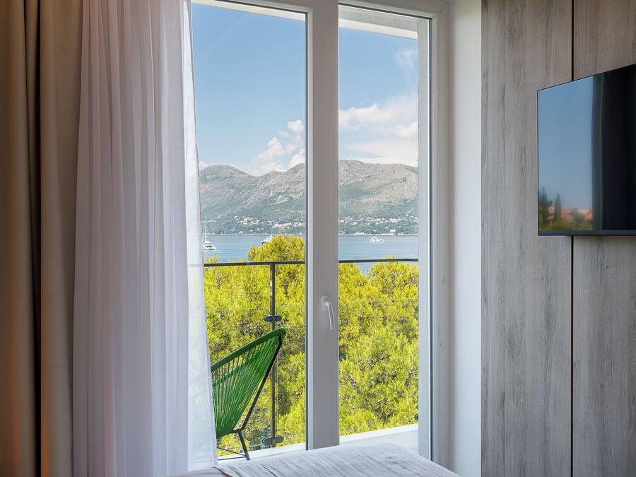 A room with a large window, a green chair, and a flat-screen TV mounted on the wall.