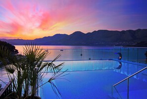 A pool with a glass barrier, surrounded by mountains and a sunset. - Hotel Cavtat (Konavle)