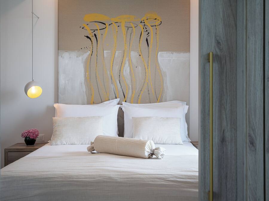 A neatly made bed with white linens, a bedside lamp, and a wall with abstract art.