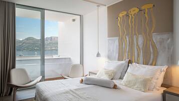 Een moderne hotelkamer met een groot bed, een stoel, een nachtkastje en uitzicht op zee en bergen.