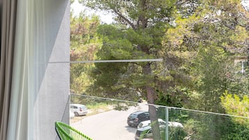 A balcony with a green chair, a small table, and a view of parked cars and trees.