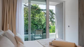 Quarto com uma cama grande, vista para uma varanda com cadeira e porta de vidro que dá para uma área externa.