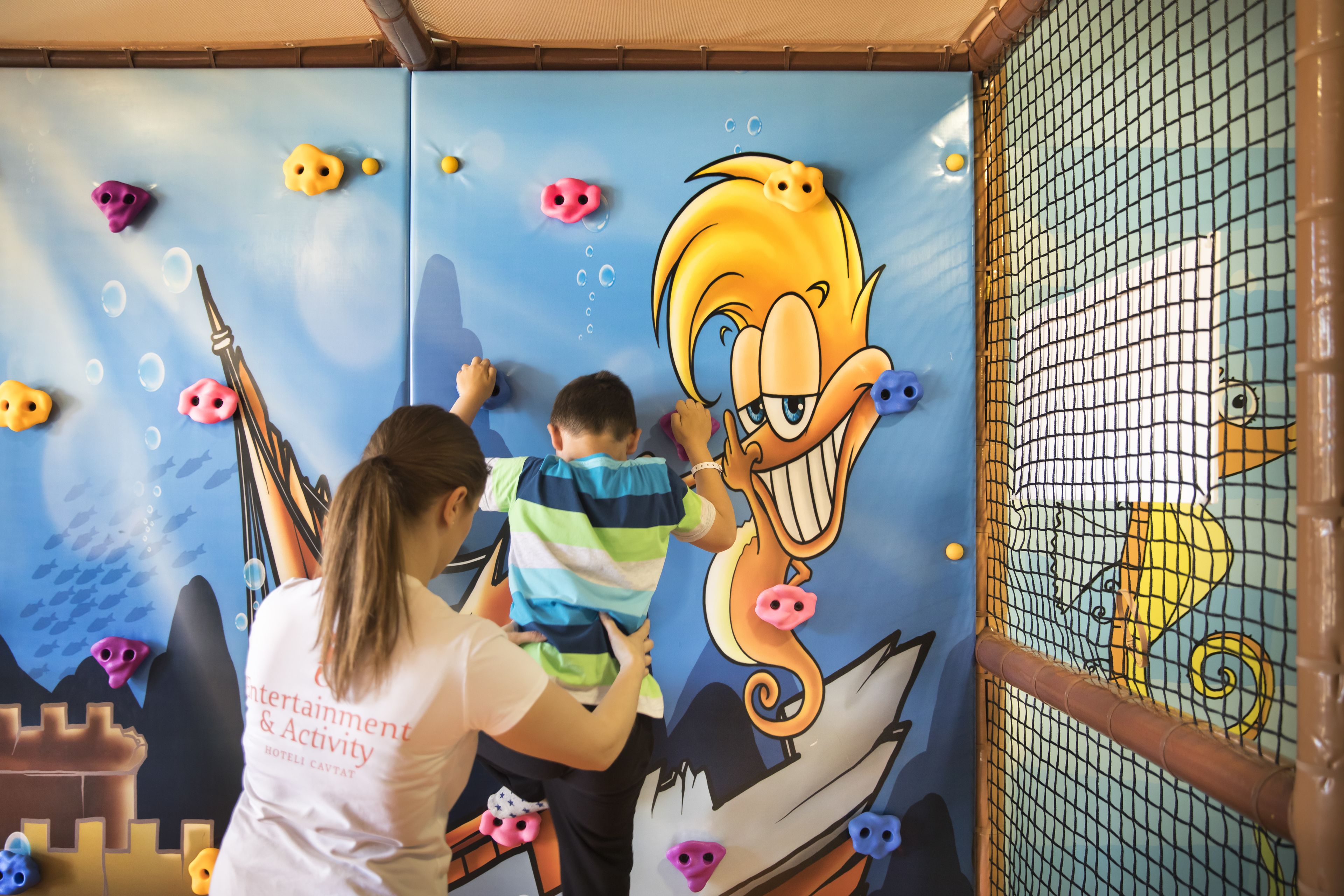A child climbing on a wall with cartoon characters and climbing holds.