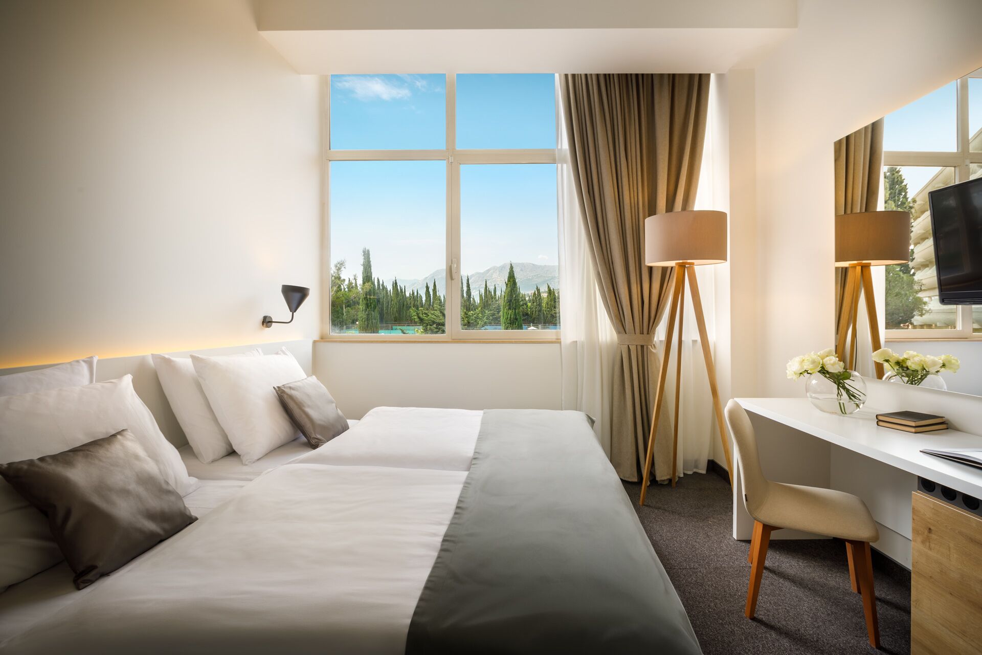 Habitación de hotel con cama, escritorio, silla y un ventanal con vistas a árboles y montañas.