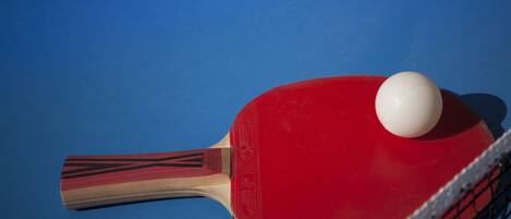 Una paleta de ping pong con una pelota roja y blanca sobre una mesa azul.