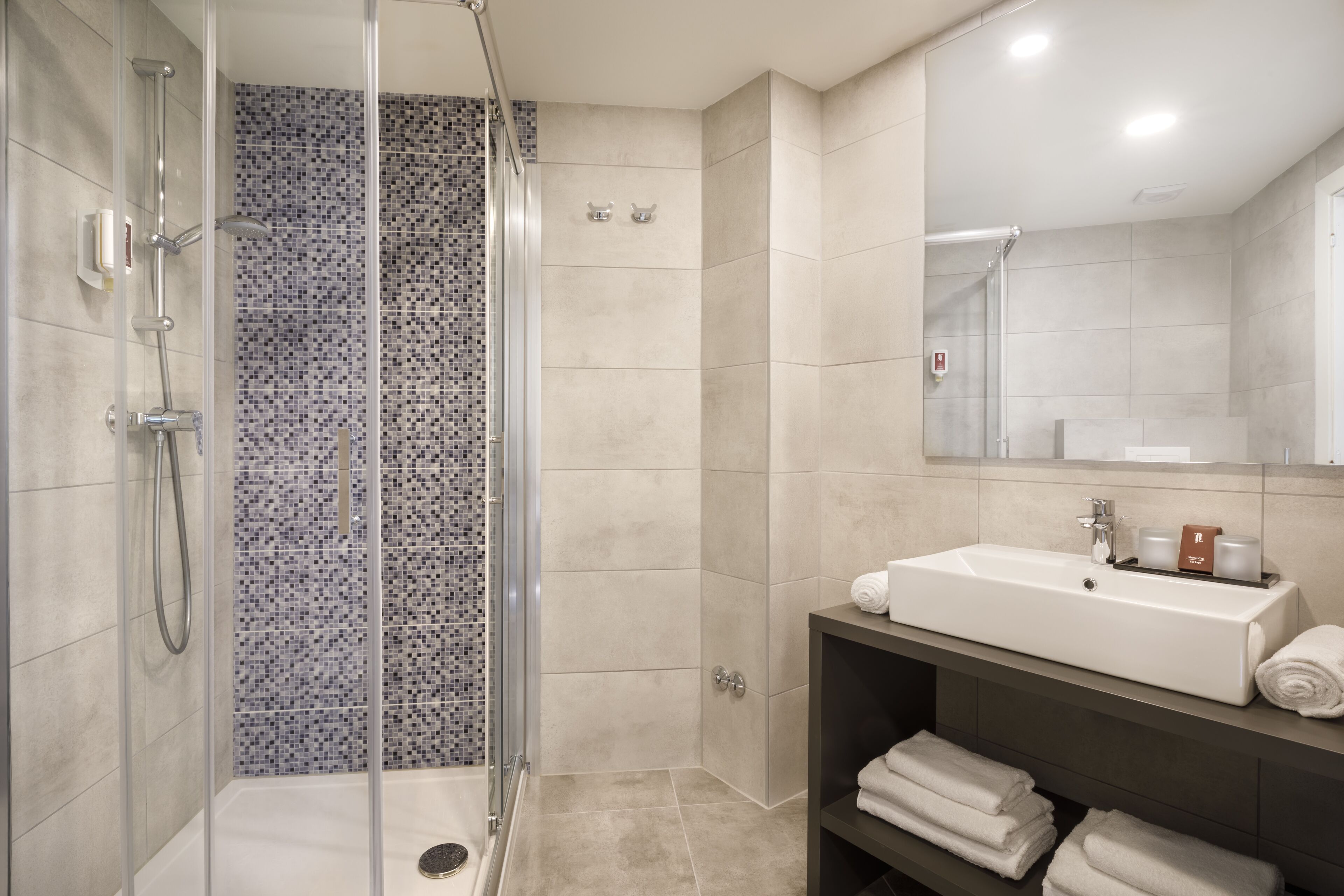 A modern bathroom with a glass-enclosed shower, a sink with a mirror above it, and neatly folded towels on a shelf.