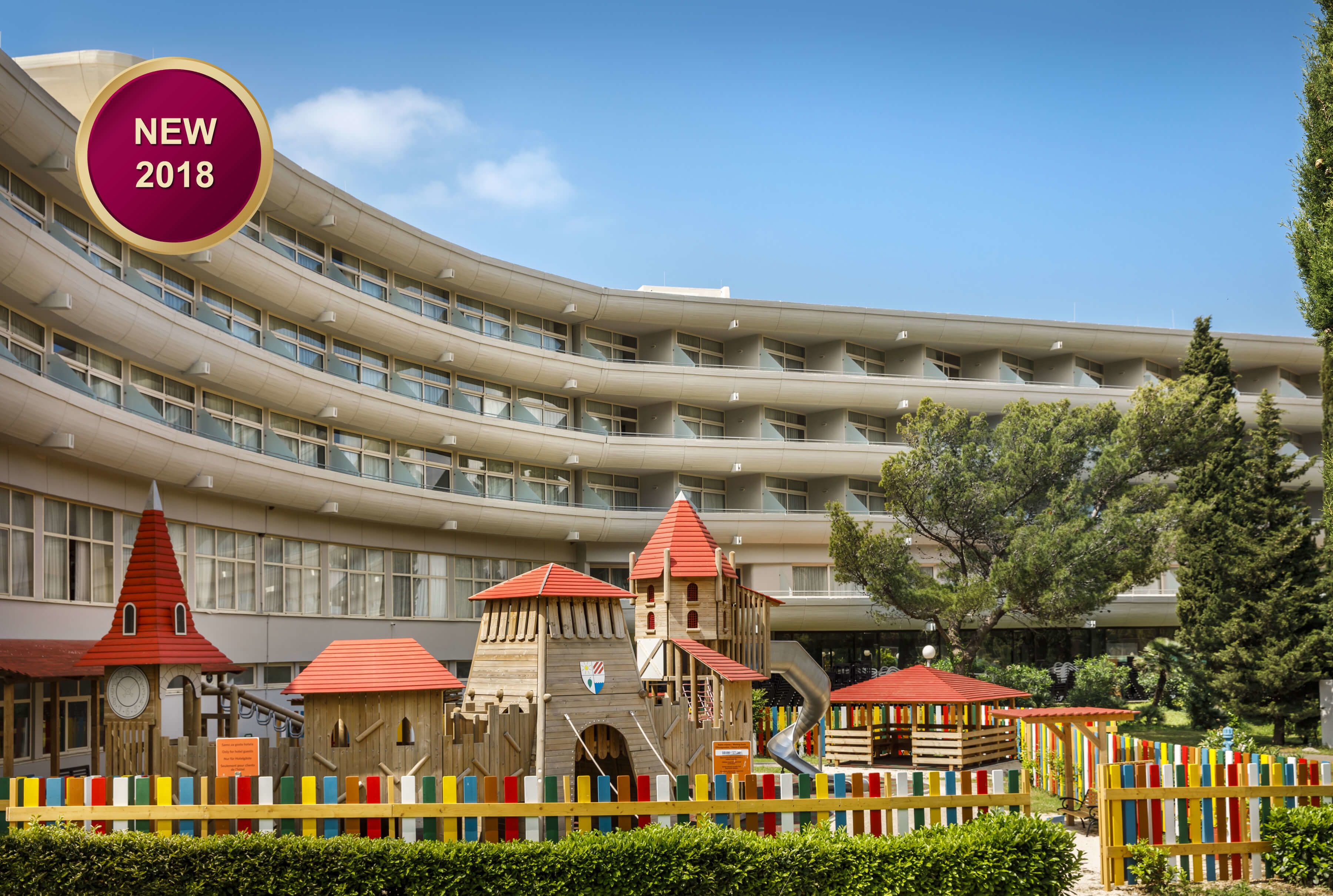 A modern hotel with a curved facade, multiple balconies, and a playground area with colorful play structures.