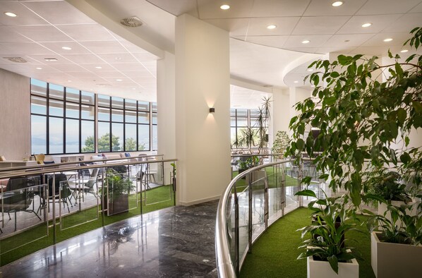 A modern office space with a curved glass railing, green artificial grass, and large windows offering a view of the outdoors.