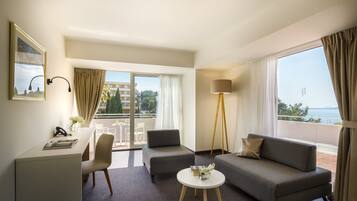 Quarto de hotel moderno com varanda, uma escrivaninha, dois sofás e um abajur.