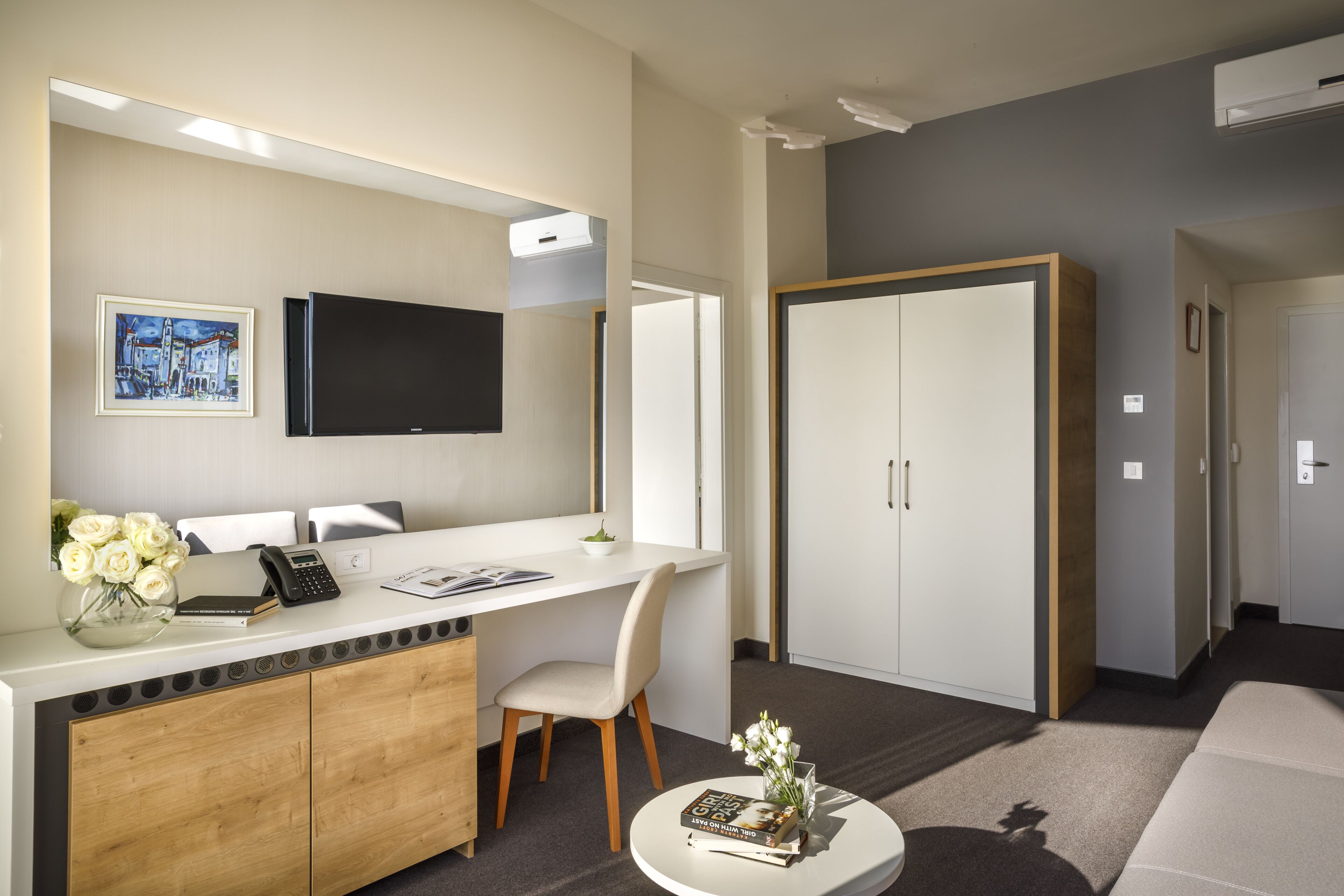 A modern hotel room with a desk, chair, and a large wardrobe.