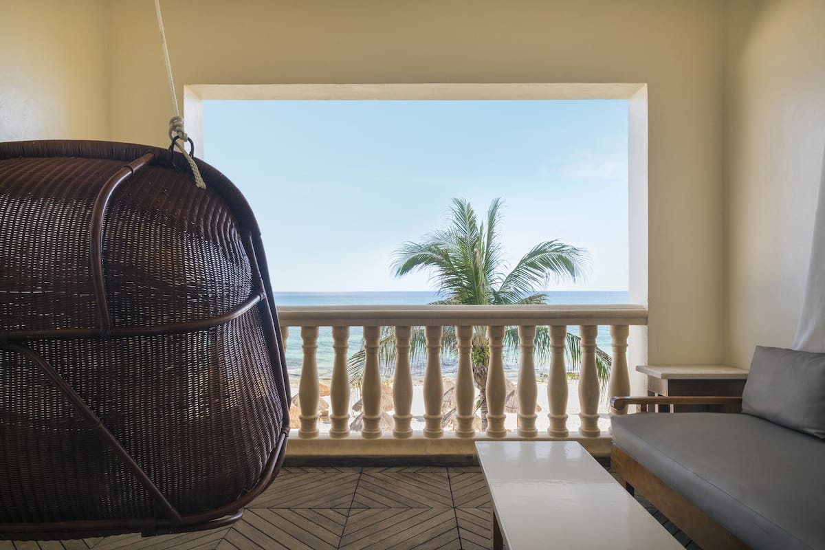 A balcony with a wicker chair, a sofa, and a view of the beach.