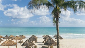 A beach with thatched umbrellas and lounge chairs, a palm tree, and the ocean. - JOIA Paraíso by Iberostar - Adults Only - All Inclusive (Playa del Carmen)