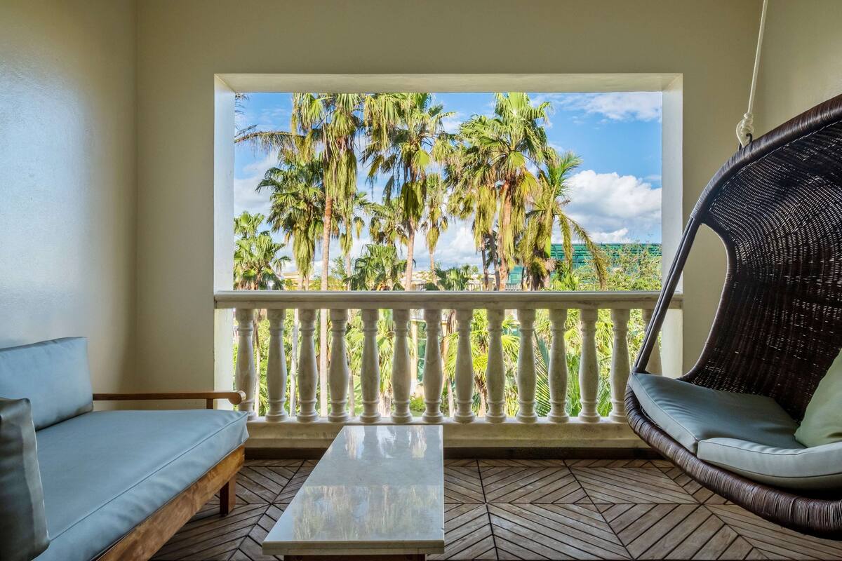 A balcony with a view of palm trees, a wicker chair, a sofa, and a small table.