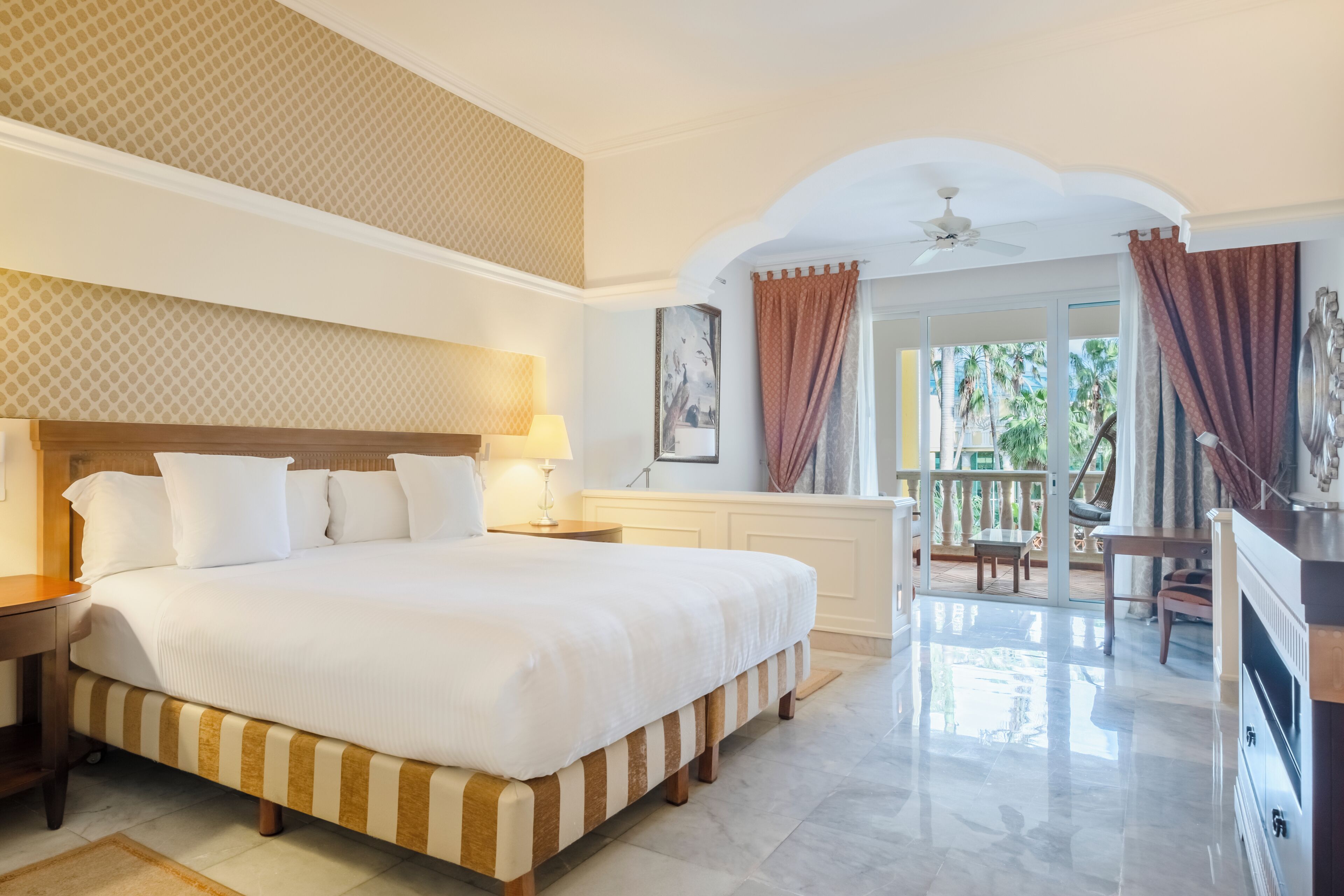 A hotel room with a large bed, a ceiling fan, a balcony with a view, and a TV.